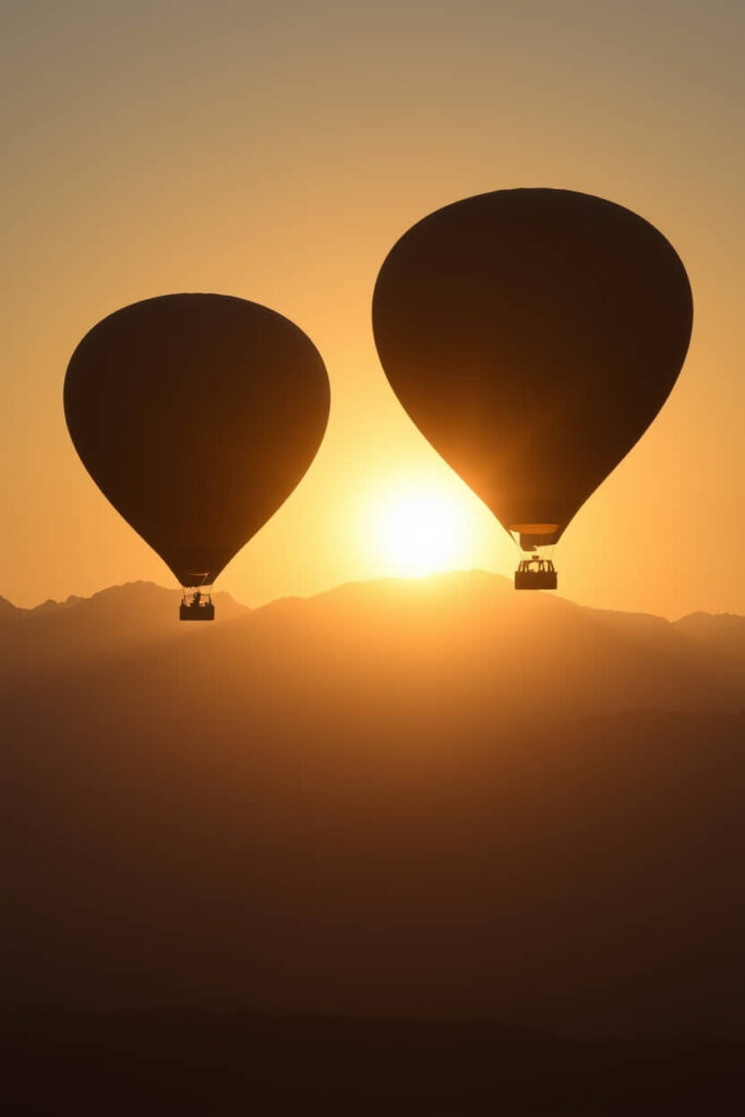 Silhouetted hot air balloons against a sunrise over the Alps